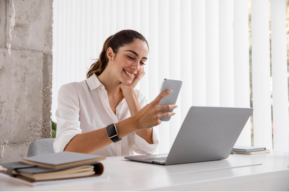 Mujer sonriendo con el celular y la laptop mientras envía dinero de México a Brasil con el Dulloo